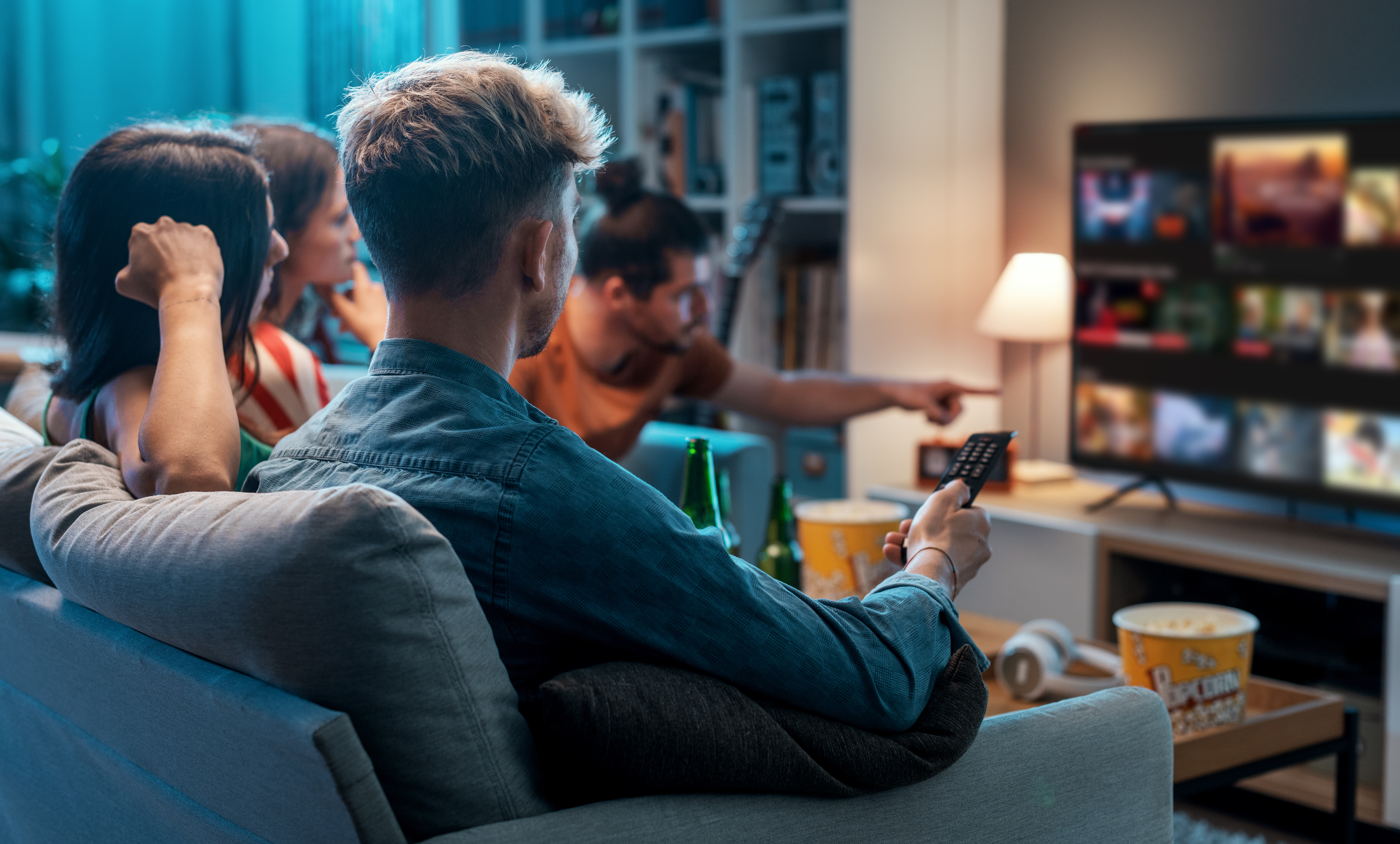 Junge Menschen sitzen auf dem Sofa und schauen Streaming-Angebote auf dem Smart-TV