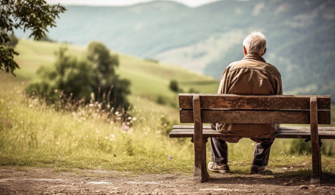 Mann sitzt auf Bank und schaut in die Natur