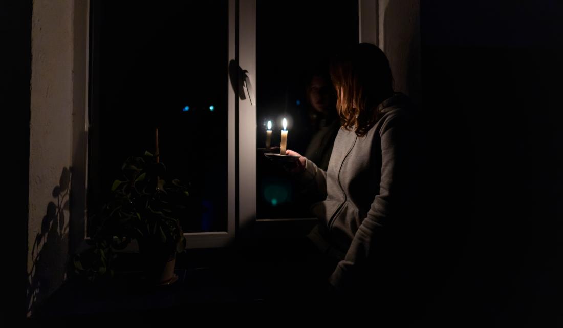 Frau steht mit Kerze am Fenster
