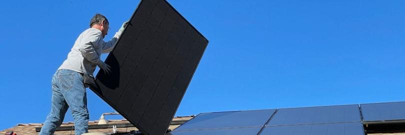 Mann mit PV-Modul auf Dach