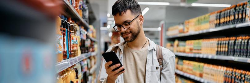 Mann kauft im Supermarkt ein unf schaut auf sein Smartphone