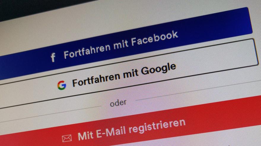 Ein PC-Monitor zeigt den Login-Bereich einer Internetseite mit Buttons für Facebook-Login, Google-Login und Anmeldung per E-Mail