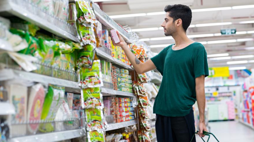 Ein Mann kauft im Supermarkt ein und studiert eine Verpackung