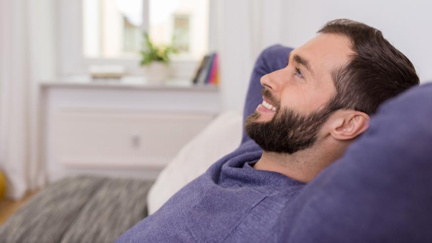 Ein Mann sitzt entspannt auf einem Sofa im Wohnzimmer.