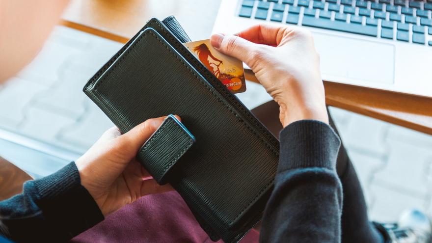 eine junge Frau mit Portemonnaie und Kreditkarte or einem Laptop