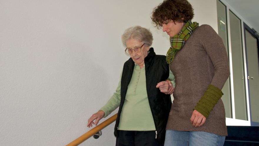 Eine junge Frau hilft einer älteren die Treppe hinab.