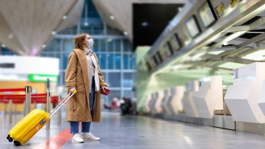 Frau mit Maske steht ahnungslos in leerem Flughafen