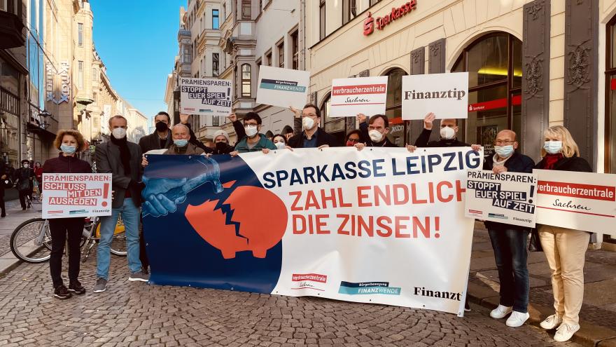 Menschen protestieren zum Weltspartag vor einer Sparkasse