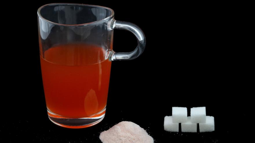 Ein Glas ist mit einer Flüssigkeit gefüllt, davor liegt ein Haufen Zucker und Würfelzucker