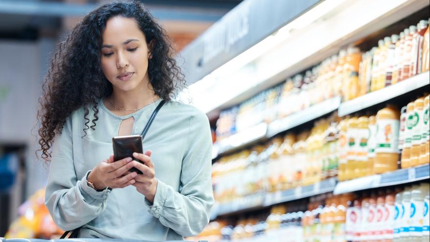 Eine Frau nutze eine Supermarkt-App auf ihrem Handy beim Einkaufen
