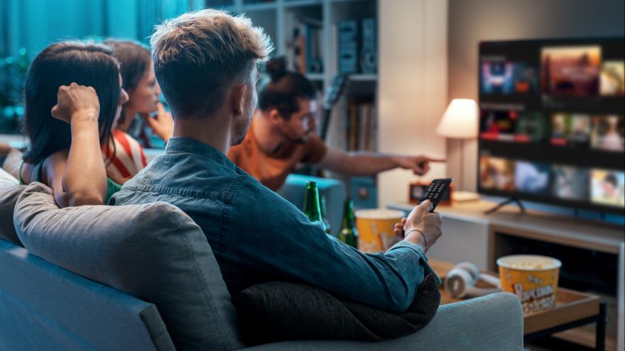 Junge Menschen sitzen auf dem Sofa und schauen Streaming-Angebote auf dem Smart-TV