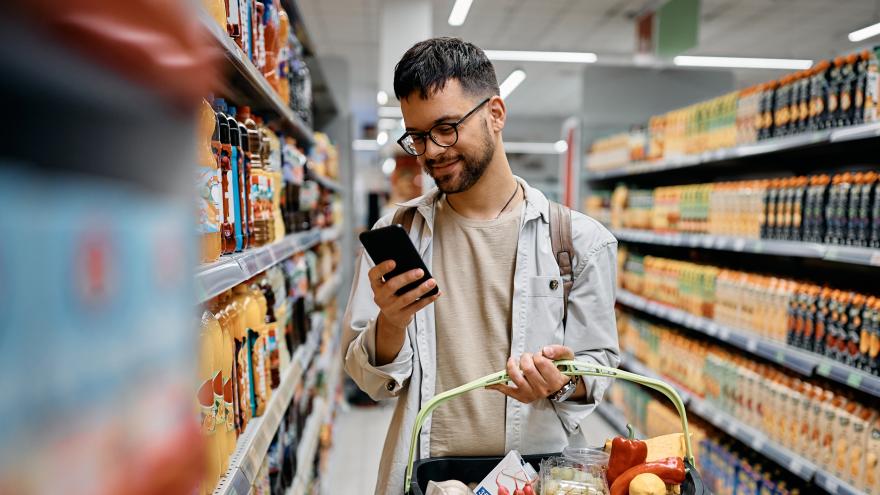 Mann kauft im Supermarkt ein unf schaut auf sein Smartphone