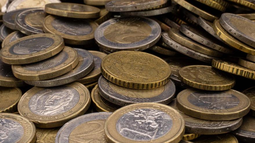 Eine Nahaufnahme zeigt einen großen, ungeordneten Haufen verschiedener Euro-Münzen, die übereinandergestapelt sind. Im Vordergrund sind deutlich 1-Euro- und 2-Euro-Münzen sowie goldfarbene Cent-Stücke (wahrscheinlich 50 Cent) zu erkennen. Die Münzen weisen Gebrauchsspuren und eine matte Textur auf, wobei das Licht die geprägten Ränder und Oberflächendetails hervorhebt.