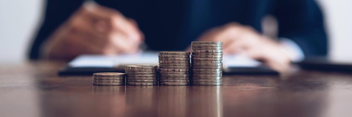 Eine Person notiert sich etwas hinter vier verschieden hohen Stapeln von Geldmünzen.