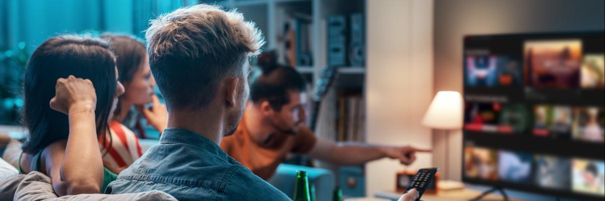 Junge Menschen sitzen auf dem Sofa und schauen Streaming-Angebote auf dem Smart-TV