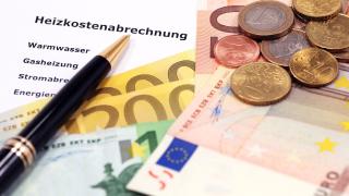 Auf einer Heizkostenabrechnung liegen Euroscheine und -Münzen und ein Kugelschreiber.
