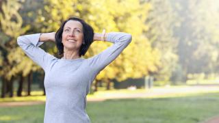 Eine Frau über 50 stretcht sich beim Sport in einem Park